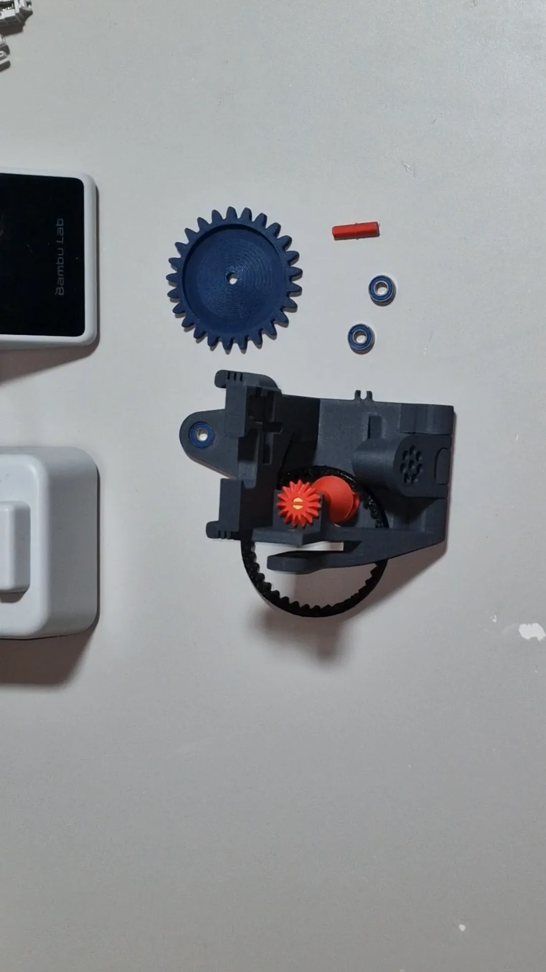 A printed mechanism body with the belt and a bevel gear fitted, and the transfer wheel, two bearings and the axle beside it